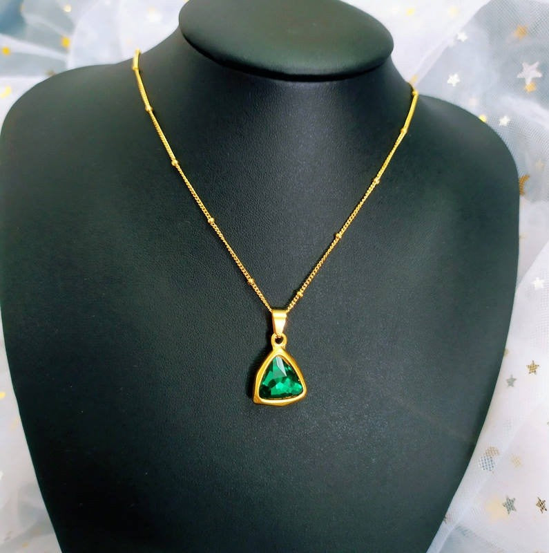 A gold chain necklace with a triangular green gemstone pendant, displayed on a black jewelry bust.
