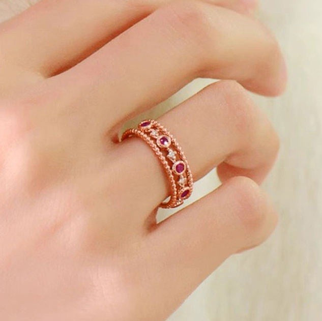 A close-up of a hand wearing a rose gold double-band ring decorated with small round pink gemstones.