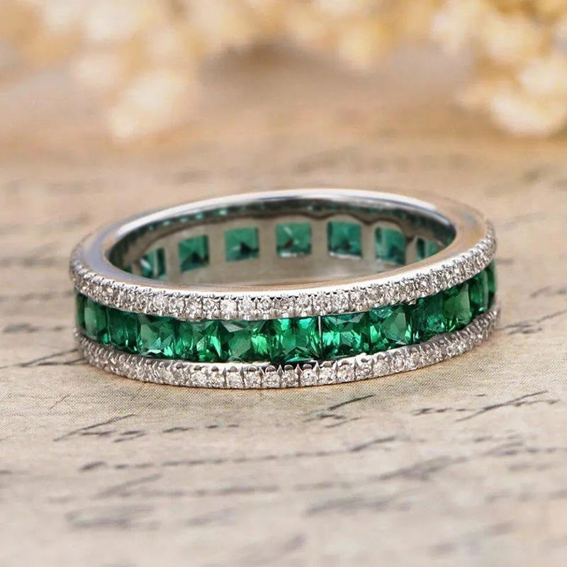 Two emerald rings with diamond accents on a textured surface