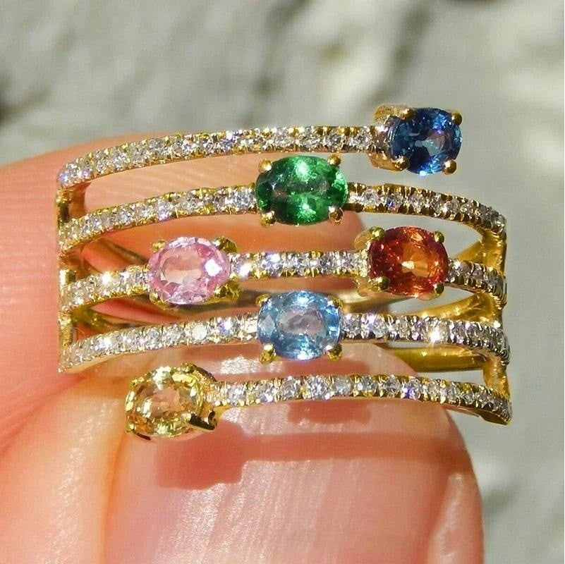 a gold ring with multi coloured gemstones on a grey background