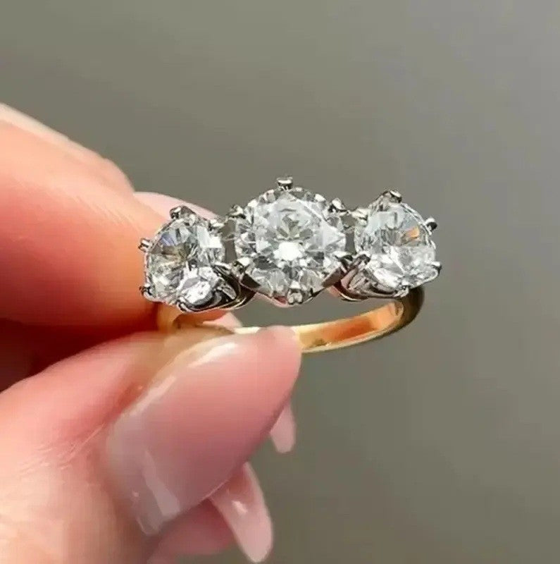 Gold ring with three diamonds held by a hand against a neutral background