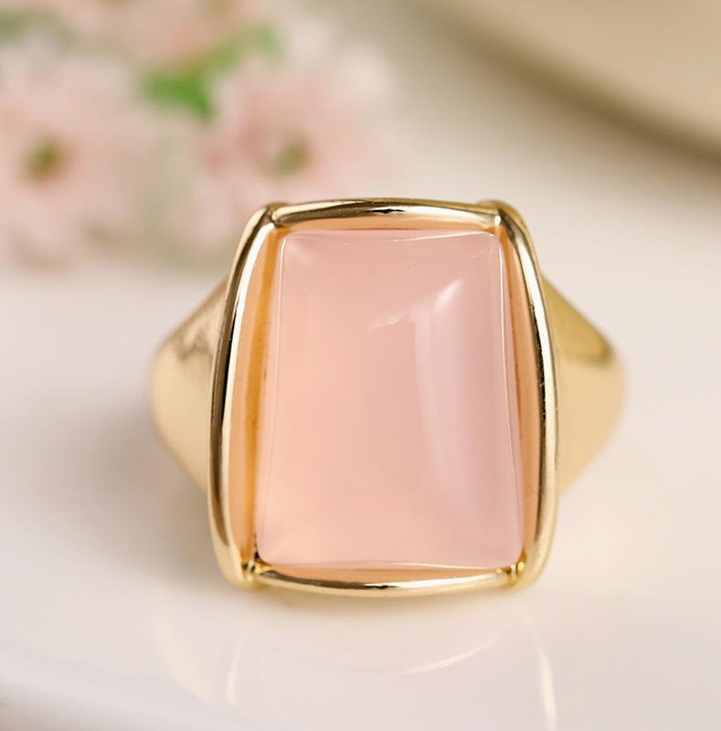 A gold signet ring featuring a large, smooth, rectangular pale pink stone