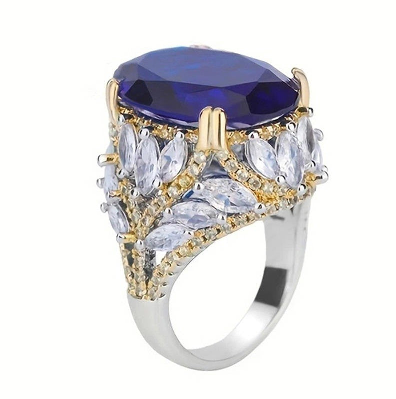 A two-tone silver and gold ring featuring a large oval deep blue gemstone on top, surrounded by marquise-cut clear crystals and small gold accents on a white background.