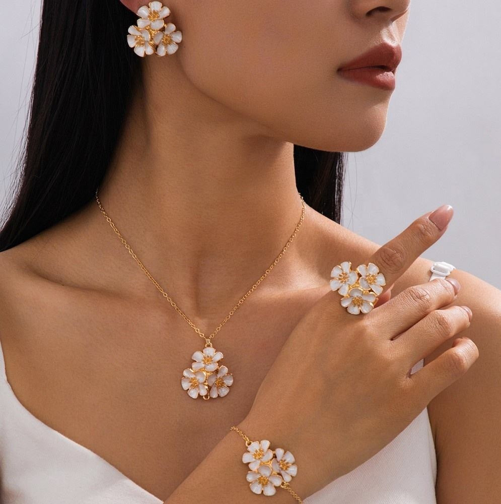 A close-up lifestyle shot of a model wearing a matching gold jewelry set featuring white flower-shaped charms with gold centers, including a necklace, earring, ring, and bracelet.