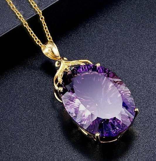 A gold pendant necklace featuring a large, faceted oval purple gemstone, displayed on a textured black background.