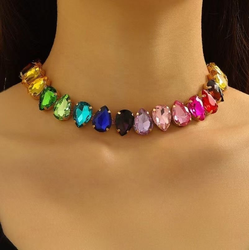 A multicolor rhinestone choker necklace displayed on a mannequin neck. The necklace features a row of teardrop-shaped clear rhinestones in various colors including yellow, green, blue, pink, purple, and red, set in gold-toned metal.