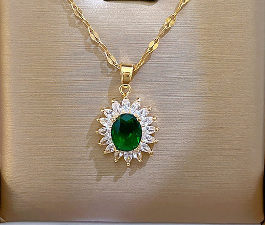 A gold pendant necklace featuring a central oval green gemstone surrounded by a halo of small clear stones, displayed on a textured beige jewelry box.