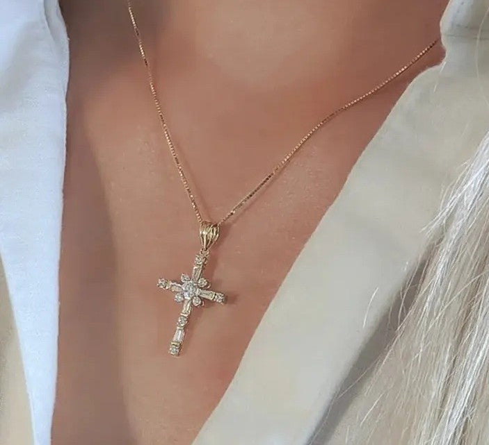 A gold cross pendant necklace with clear stones, worn on a model's neck over a white collared shirt.