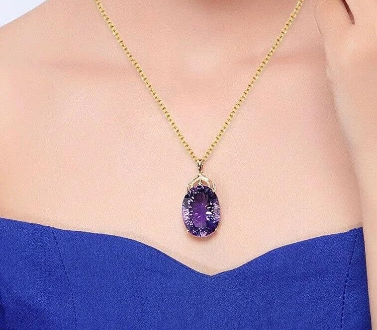 A gold chain necklace with an oval purple gemstone pendant, worn by a model in a blue strapless top.