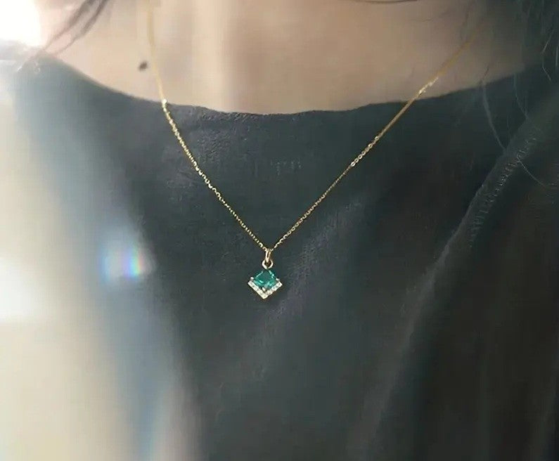 A gold pendant necklace featuring a square-cut green gemstone 
