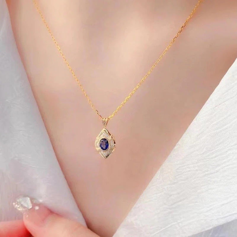 A delicate gold chain necklace with an evil eye pendant featuring a dark blue gemstone, worn on a model's neck over a white textured top.