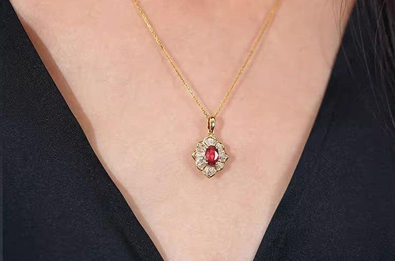 A close-up of a person wearing a delicate gold chain necklace with a central oval red gemstone surrounded by small clear stones in a gold setting.