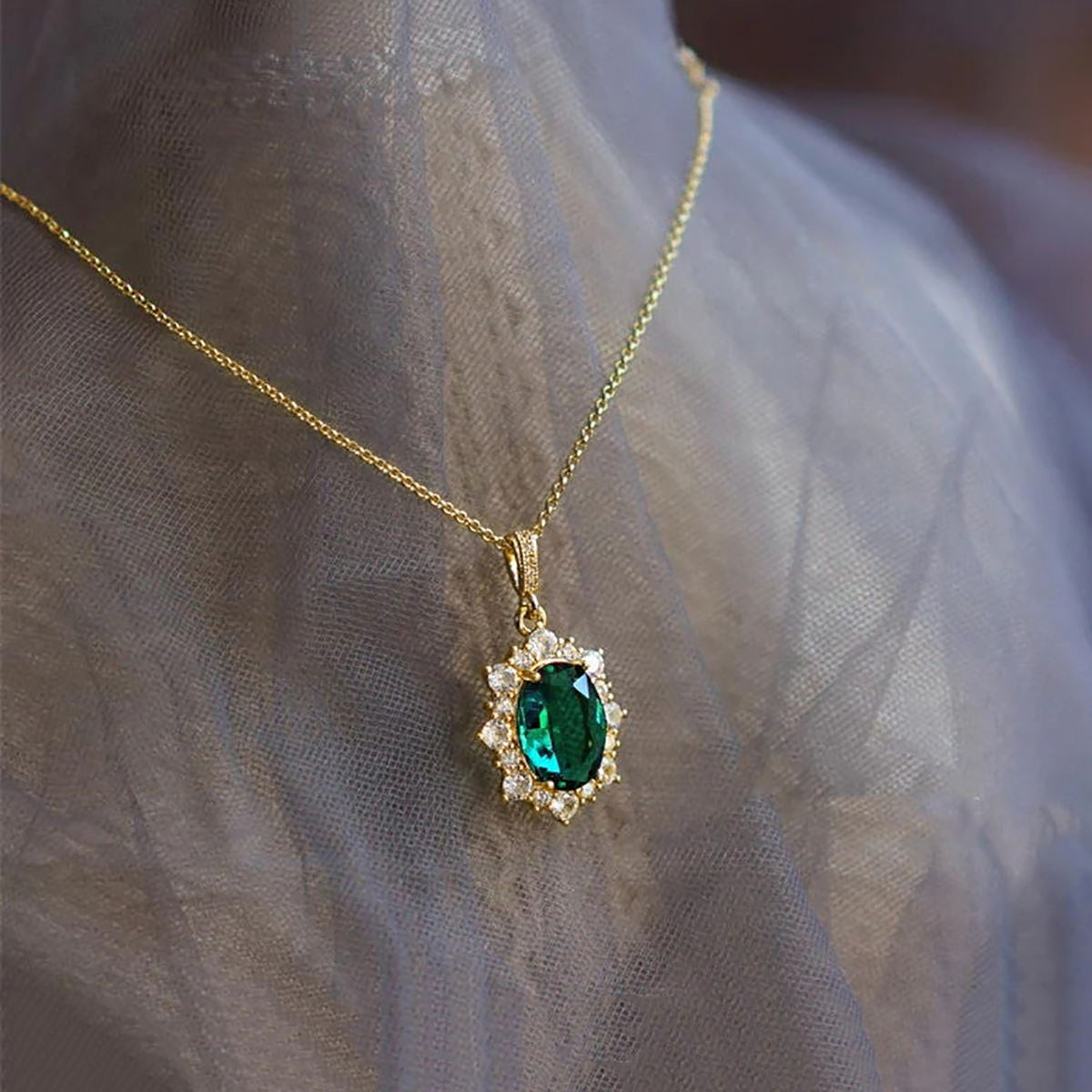 A gold pendant necklace with an oval green emerald-cut center stone