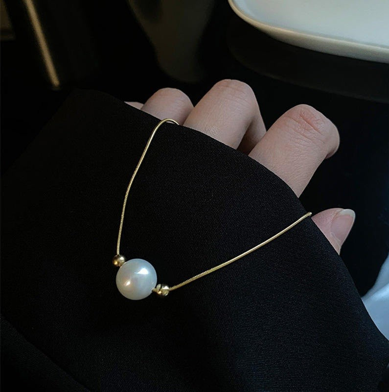 Gold bracelet with a pearl on a person's wrist against a dark background