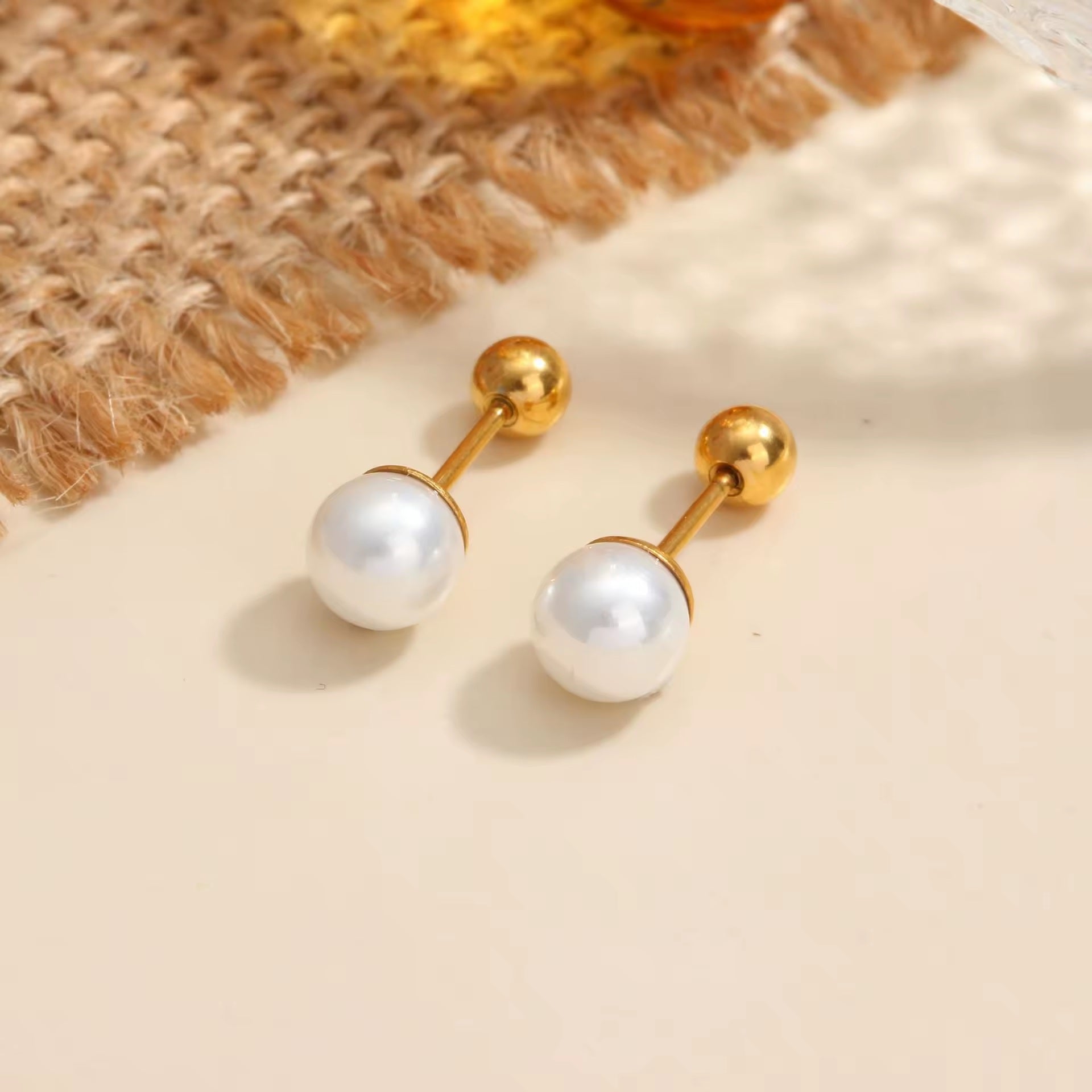 Pair of pearl earrings with gold posts on a textured beige surface