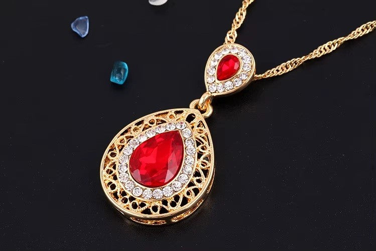 Gold necklace with a red teardrop pendant on a black background