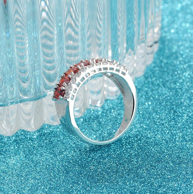Silver ring with red gemstones on a blue glittery background