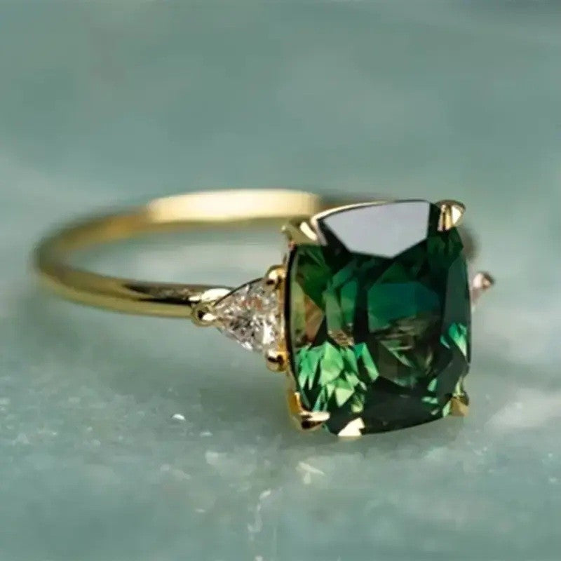 Gold ring with a large green gemstone on a light blue background