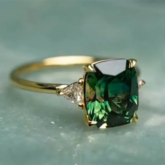 Gold ring with a large green gemstone on a light blue background