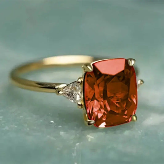 Gold ring with a large red gemstone and smaller diamond on a light blue background