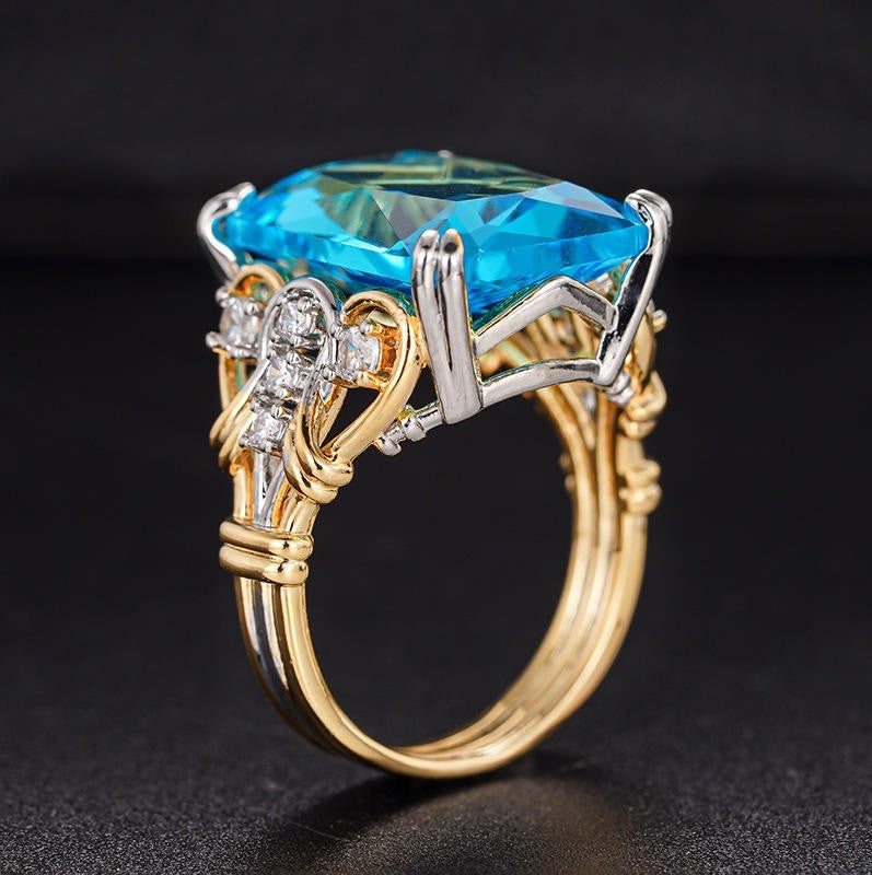 A yellow gold ring with a large rectangular blue gemstone and silver accents, set against a dark background.