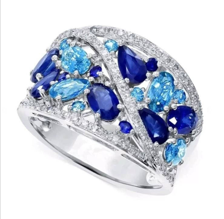 A silver-tone ring featuring a wide, openwork band set with deep blue oval and pear-cut gemstones, light blue marquise-cut gemstones, and small clear accent stones, shown on a plain white background.