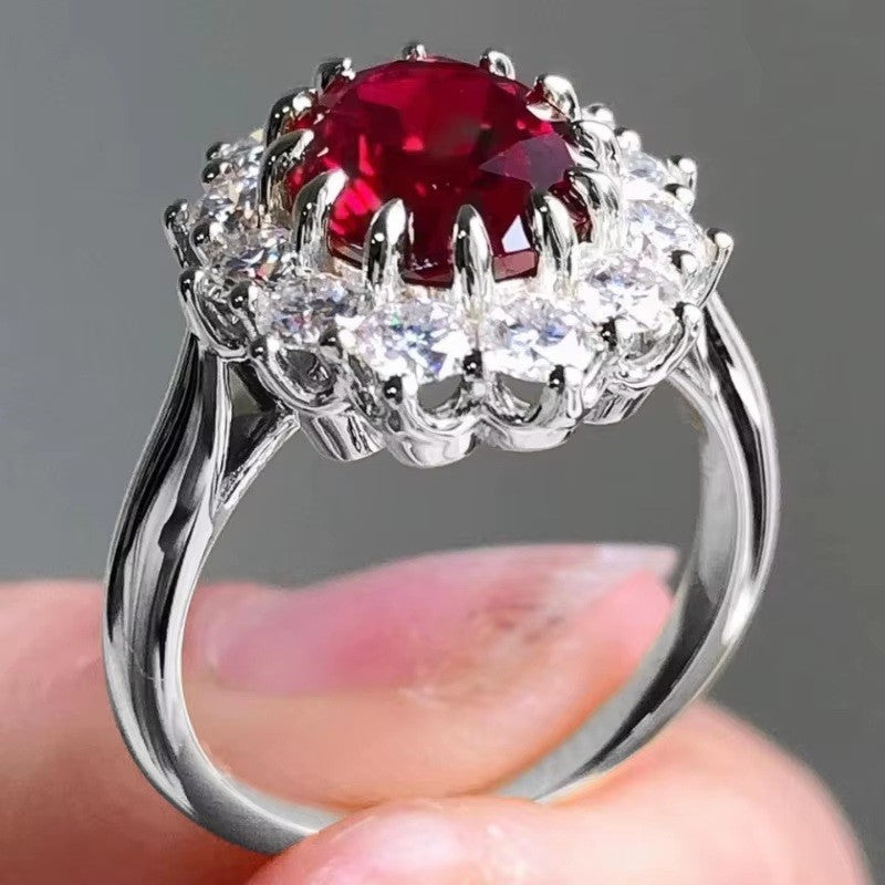 Silver ring with a red gemstone held by a hand against a gray background
